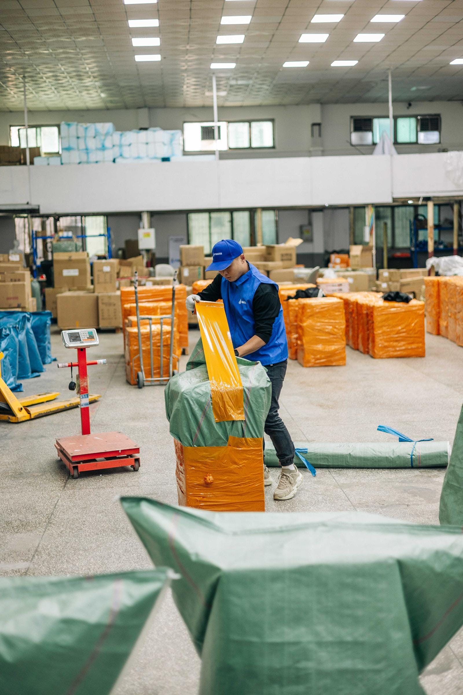 Співробітник OptMaster у синій формі пакує консолідований вантаж на складі в Гуанчжоу, Китай.