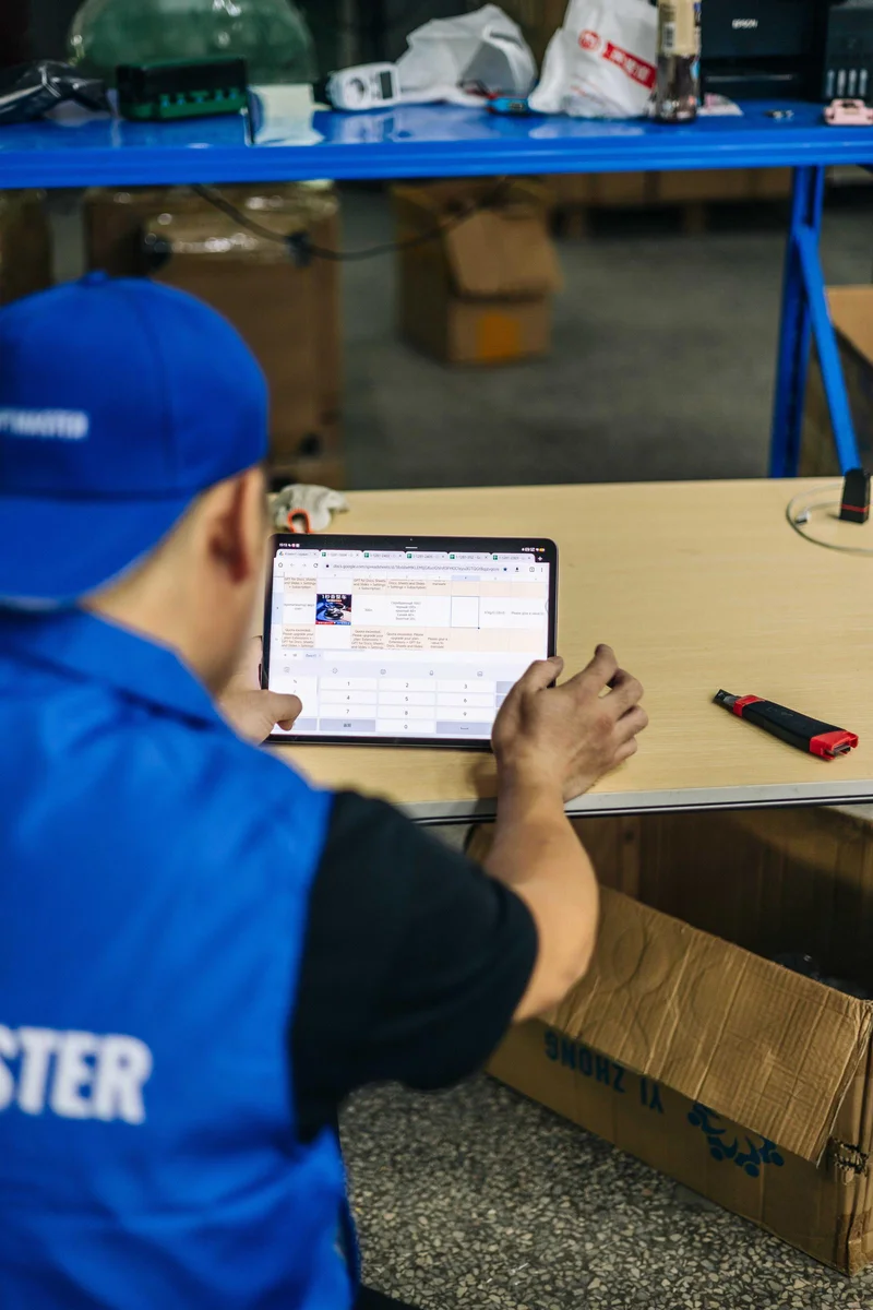 Працівник OptMaster у синій формі обробляє дані замовлень на планшеті на складі в Гуанчжоу.