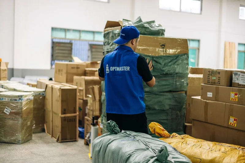 Працівник OptMaster у синьому жилеті сортує вантажі на складі в Гуанчжоу для доставки з Китаю в Україну.
